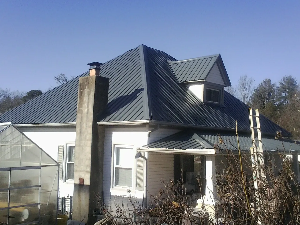 Dark blue standing seam metal roof on a white farmhouse with dormer — Slate & Tile Roof Repair by Roofing Brothers in Berry