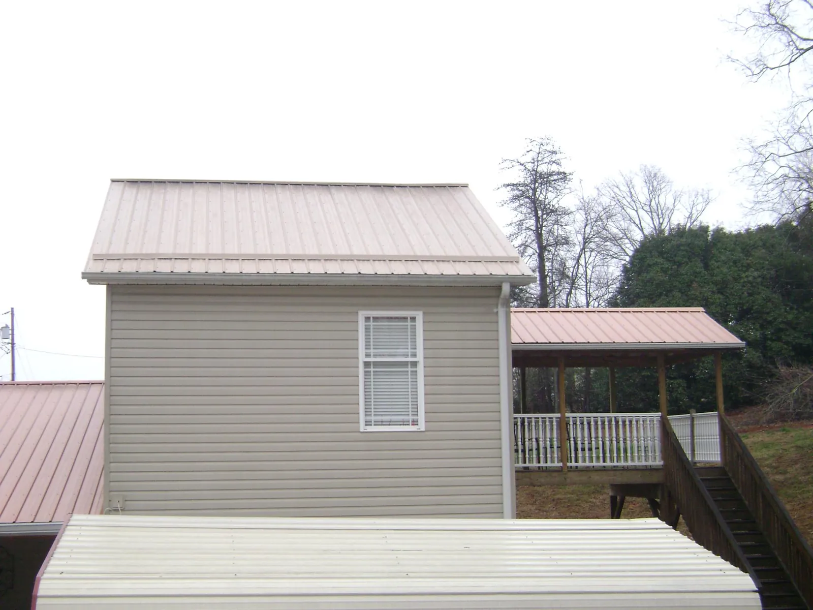 Tan metal roofs on a two story addition and attached porch, from a Roof Replacement job in Berry